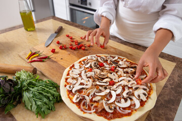 Close-up on the hands of the chef adding tomatoes to the pizza toppings. Vegan food.