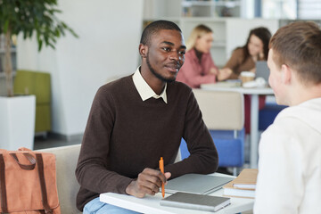 Wall Mural - Portrait of young African-American man talking to friend across table while studying together in college library, copy space