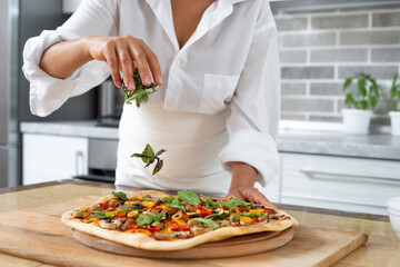 The cook sprinkles the pizza with basil herbs from above. Falling leaves are visible. Vegan food.