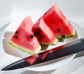 knife and pieces of watermelon laid out on a white plate on the background of a white table. harvest concept, vitamins tasty and healthy food.