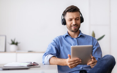 Wall Mural - Handsome Businessman In Headphones Relaxing At Workplace With Digital Tablet, Having Break