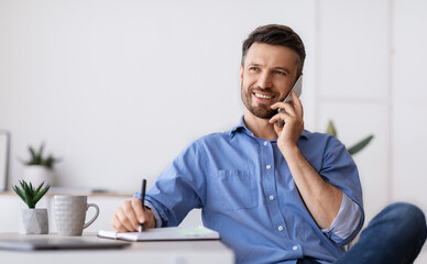 Wall Mural - Business Communication. Successful Businessman Sitting At Workplace Talking On Cellphone With Client