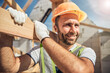 Positive delighted young constructor carrying wooden beam