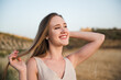 Portrait of smiling young woman touching her hair relaxed in field. Happy girl enjoying her holidays alone