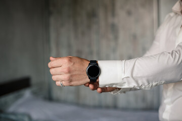 A man elegant businessman buttons a watch on his hand he is dressed in a white dress shirt