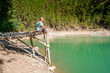 © KseniaJoyg - Younf blond man on a bridge above a mountain lake with clear water and a view of a green forest. Copy space