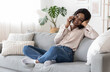 © Prostock-studio - Mobile Communication. Cheerful african woman talking on cellphone with friends at home