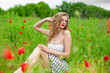 A young long-haired girl enjoys the colors of nature on a blooming poppy field on a hot summer day