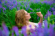 Beautiful young blonde girl in a green field among purple wildflowers. Wildlife beautiful girl