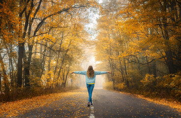 Wall Mural - happy young woman on the road in beautiful autumn forest in fog at sunset. landscape with alone girl