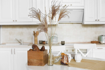 Cozy interior of a light kitchen. Kitchen table with kitchen utensils, two cups, a jar of sweets and a box of cookies