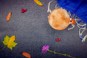 Wall Mural - Cup of coffee cappuccino with cinnamon, blue stole, autumn leaves, Rowan berries, flower on a black background with copy space, top view, flat lay. Beautiful autumn composition, beautiful background.