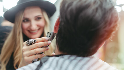 Barber woman trimming beard of client with the machine