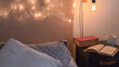© Pablo - Leer un libro antes de irse a dormir en una cálida y confortable habitación iluminadas por pequeñas luces. Primer plano de una mesa de noche junto a un par de libros y una taza de café.