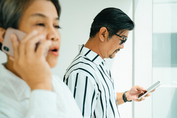 Wall Mural - Side view of senior couple using smartphone at window.