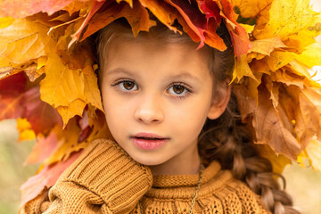 Wall Mural - A little girl in an autumn sweater and a maple wreath.