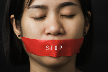 Wall Mural - Asian woman blindfold wrapping mouth with red adhesive tape on black background. Freedom speech censorship and stop talk, International Human Right day