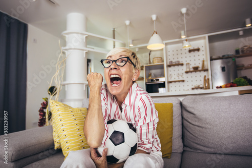 Elderly woman emotionally watching soccer on tv and celebrating victory at home.