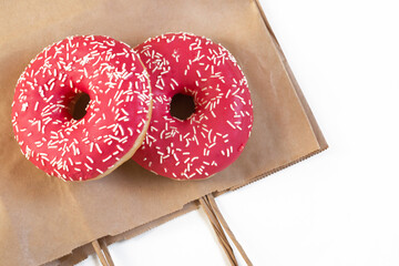 two donuts with pink icing and sprinkles on a paper bag, white background