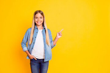 Sticker - Portrait photo of schoolgirl with blonde hair pointing with finger on blank space isolated on bright yellow color background