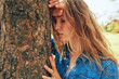 © iuricazac - Closeup image of an young woman wearing a blue denim shirt hugs a big tree, posing on nature background. Portrait of beautiful female with closed eyes has dreamy expression outdoor in the park.
