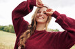 © iuricazac - Happy young blonde woman in red sweater and winter hat smiling broadly posing on nature and sky background.