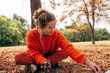© iuricazac - Pretty young woman picks chestnuts in park. Beautiful blonde female wearing an orange sweater has joyful expression resting at the autumn nature background.
