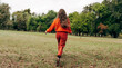 © iuricazac - Rear view of an young woman walking with blowing long blonde hair wearing an orange sweater, posing on the nature background. Pretty female playing with her hair outdoor in the park.