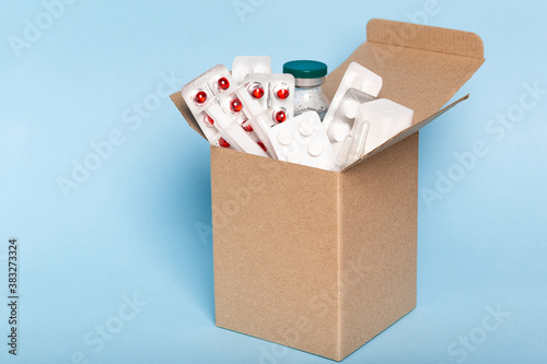 Delivery of medicines home from the pharmacy. Cardboard box with medicines, pills, bottles, injections isolated on blue background.