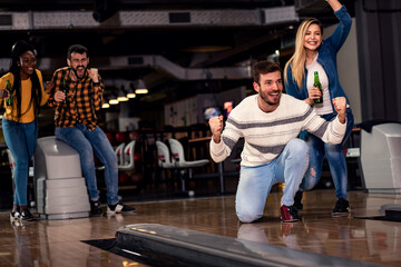 Wall Mural - Group of friends enjoying time together laughing and cheering while bowling at club.