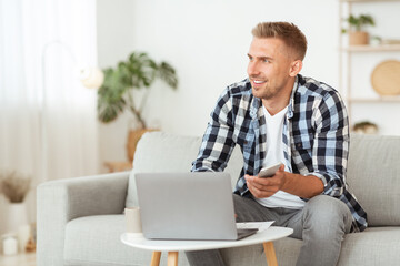 Portrait of man sitting on sofa using phone and pc