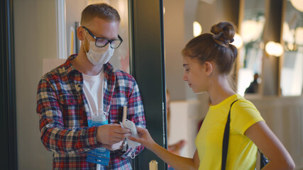 Young male teacher standing at school entrance giving safety mask to student