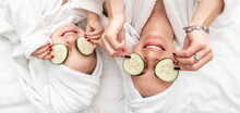 Positive Mother And Daughter Doing Face Mask Applying Pieces Of Cucumber To Their Eyes, Wrapped In A White Bath Towel, Facial Skin Care, Cosmetology And Spa