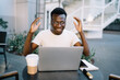 © BullRun - Happy emotional dark skinned male freelancer sitting on cafe terrace overjoyed with getting payment from online successful project, young african american man watching video celebrating victory