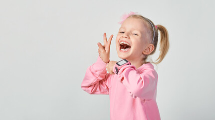 Cute caucasian little girl 4-5 year old wearing a smart watch on her wrist. Technology for children, against gray studio background