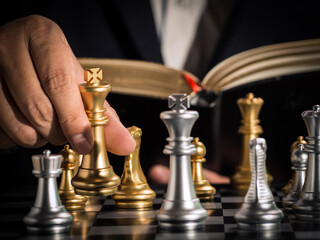 Wall Mural - Hand of businessman moving the golden king chess to fighting silver king chess with opening book guideline play successfully in the competition. management or leadership strategy and teamwork concept.