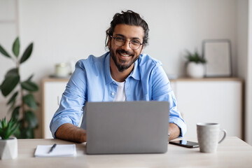 Poster - Happy Indian Freelancer Man Sitting At Desk With Laptop, Smiling At Camera