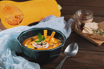 closeup pumpkin cream soup in blue plate with pumpkin seeds on wooden background, seasonal autumn dish