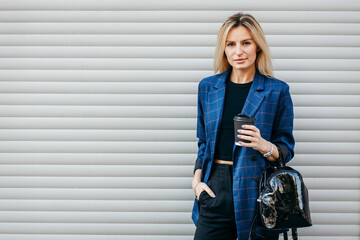 Poster - Fashion portrait of young stylish hipster woman walking on the street, wearing cute trendy outfit and drinking tasty coffee