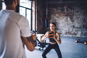 Young caucasian male and female in activewear having workout in gym throwing ball enjoying exercises, 20s woman having training with trainer keeping physical strength and muscles for slimming