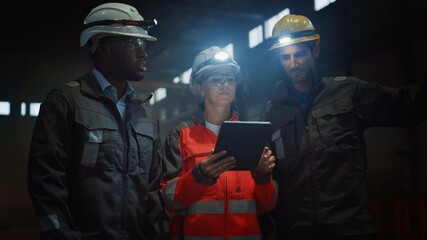 Aufkleber - Three Diverse Multicultural Heavy Industry Engineers and Workers in Uniform Stand in Dark Steel Factory Using Flashlights on Their Hard Hats. Female Industrial Contractor is Using a Tablet Computer.