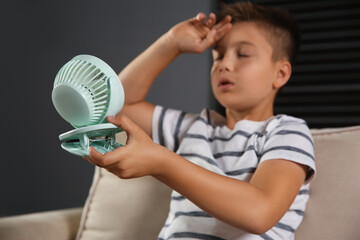 Canvas Print - Little boy with portable fan suffering from heat at home, focus on hand. Summer season