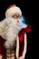 Santa Claus in a red fur coat, with a white beard and a bag of gifts posing on a black background