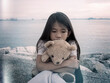 © Tanongsak - Child feeling scared. A little sad girl stay alone with her teddy bear on the sea