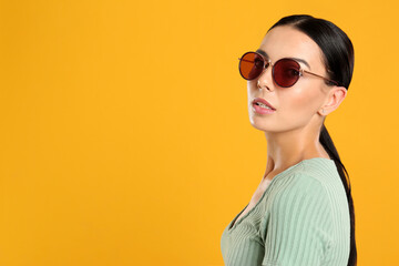 Wall Mural - Beautiful woman wearing sunglasses on yellow background. Space for text