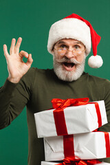 Bearded modern Santa Claus holding gifts and smiling on the green background