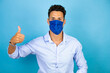 © Irene - Young handsome man wearing blue shirt over isolated blue background with mask doing the ok signal with her thumb
