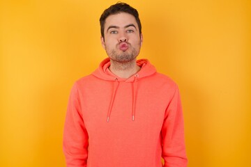 Wall Mural - Shot of pleasant looking Handsome man with sweatshirt over isolated yellow background, pouts lips, looks at camera, Human facial expressions