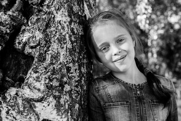 Ten-years-old girl in the woods near birch. Black and white photo.