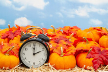 Retro Alarm Clock With Orange Pumpkins With Fall Leaves On Straw Hay With Sky